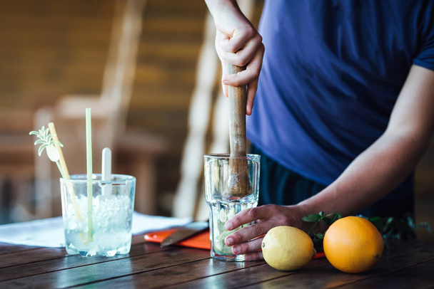 Barman prepares fruit alcohol cocktail based on lime, mint, orange, soda and alcohol - Fotoğraf, Görsel