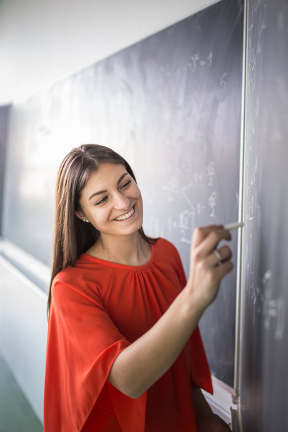 Pretty, young college student/young teacher writing on the chalkboard - Foto, afbeelding