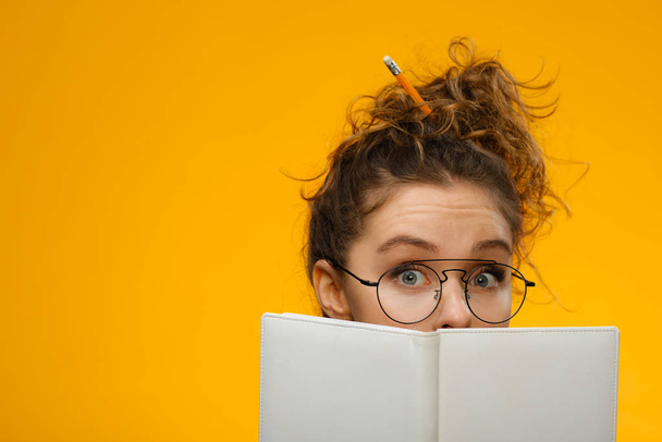Closeup portrait of teenager hiding behind notebook - Photo, Image