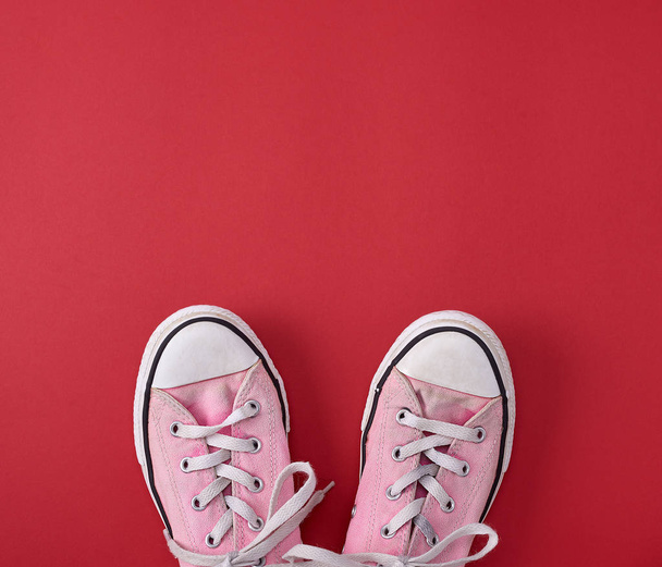pair of pink old textile sneakers with white  laces on a red background, top view, copy space - Foto, Imagem