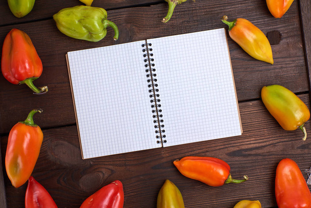 blank notepad on a brown table in the midst of fresh peppers vegetables - Photo, Image