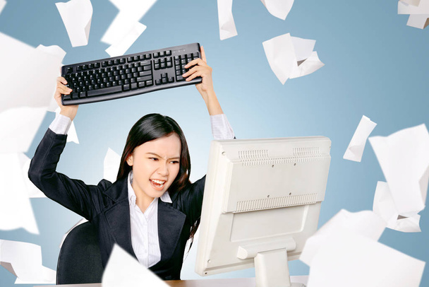 Benadrukt Aziatische zakenvrouw met vliegende papier verspreid willen dichtslaan van de computer toetsenbord op de kantoorruimte - Foto, afbeelding