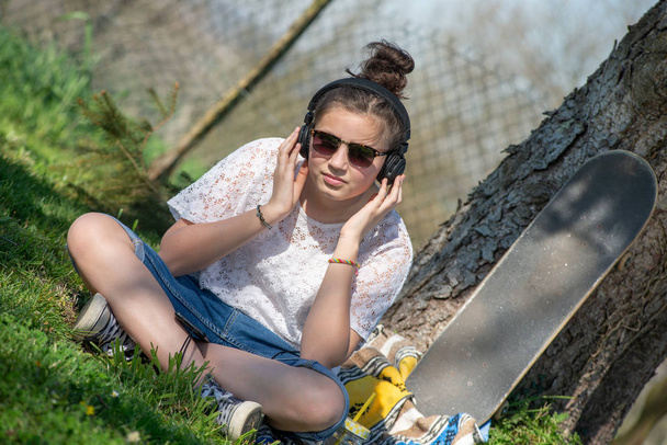 a young teenager girl listening music with headphone in the park - Foto, afbeelding