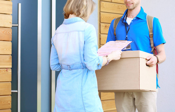 Smiling delivery man in blue uniform delivering parcel box to recipient - courier service concept. Smiling delivery man in blue uniform - Photo, Image