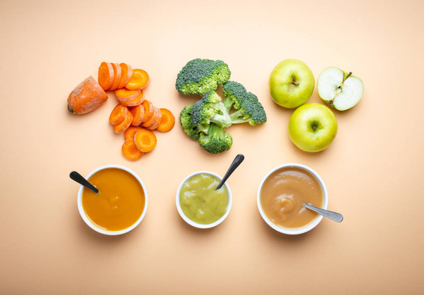 White bowls with healthy natural baby food on pastel background. Purees, made of fresh organic fruit and vegetables, flay lay, top view, concept. Food for kids made from carrot, broccoli, apples - Foto, Imagem