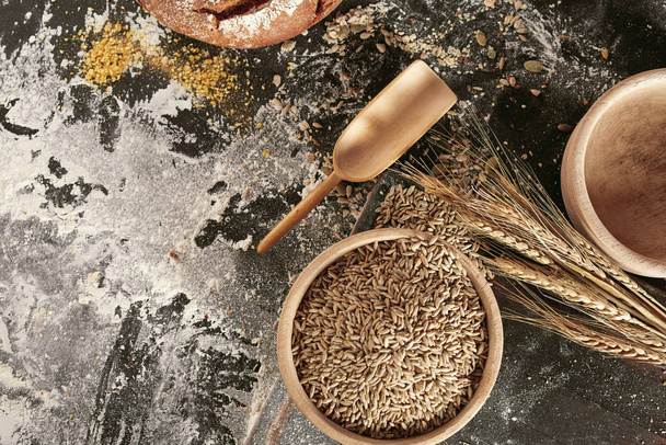Still life of ears of fresh wheat, rustic bowl of seeds and flour scattered on a kitchen table viewed top down with copy space - Foto, afbeelding