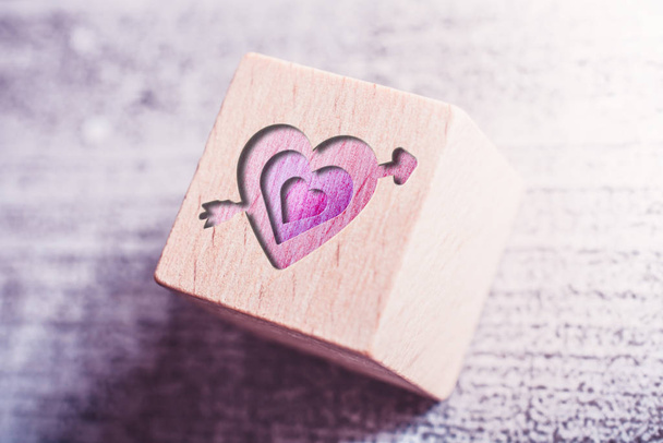 3 růžová srdce propíchnuté Amor šipka vyrytá na dřevěný blok na stole - Fotografie, Obrázek