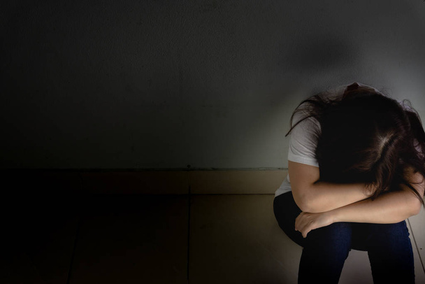 trieste vrouw omhelst haar knie en huilt alleen in een donkere kamer. Dep - Foto, afbeelding