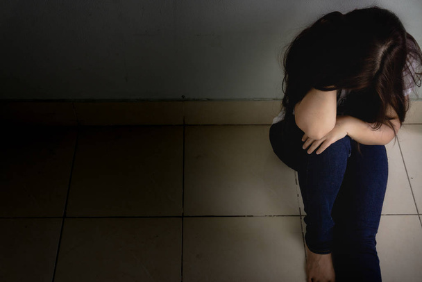 Smutna kobieta przytula kolano i płacze samotnie w ciemnym pokoju. Grupa robocza - Zdjęcie, obraz