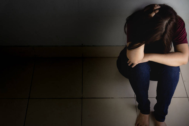 Traurige Frau umarmt ihr Knie und weint allein in einem dunklen Raum sitzend. dep - Foto, Bild