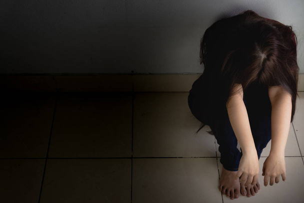 szomorú nő öleli térdét és sír ül egyedül egy sötét szobában. Dep. - Fotó, kép