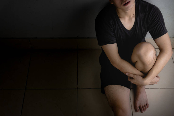 грустный мужчина обнимает колено и плачет, сидя один в темной комнате. Депре
 - Фото, изображение