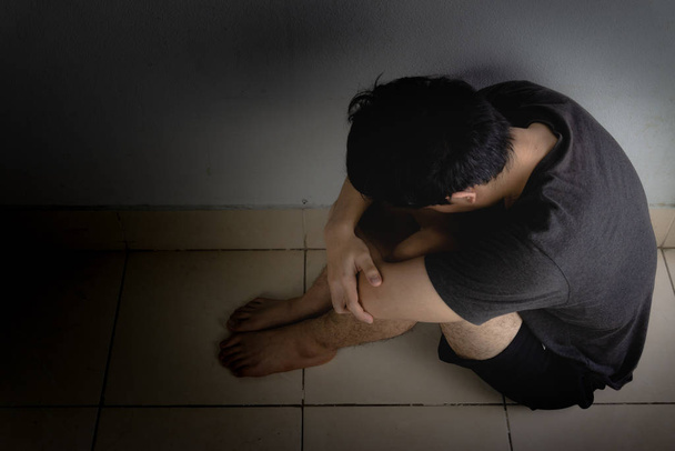droevige man omhelst zijn knie en huilt alleen in een donkere kamer. Depre - Foto, afbeelding