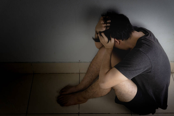 Surullinen mies halaa polveaan ja itkee yksin pimeässä huoneessa. Vähennä
 - Valokuva, kuva
