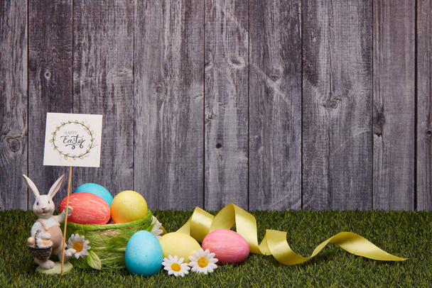 Colored easter eggs, easter rabbit and flowers lying on a green grass on a grey wooden  background with copy space. Greeting card, Easter background - Foto, Imagen