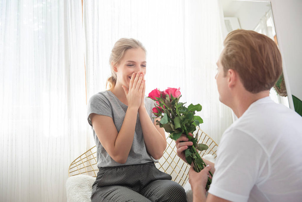 Young caucasian man surprise girlfriend with bunch of rose to celebrate their anniversary wedding day.couple have happy time together in home .Valentine day concept. - Photo, Image