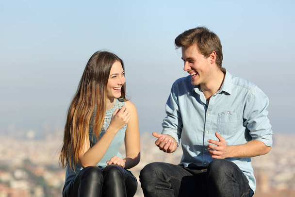 Happy couple talking sitting in a city outskirts a sunny day - Foto, Imagen
