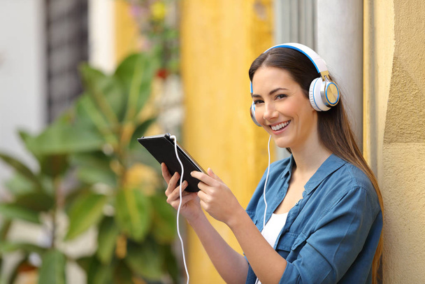Happy girl listening tablet online content looks at you in the street - Foto, Imagen