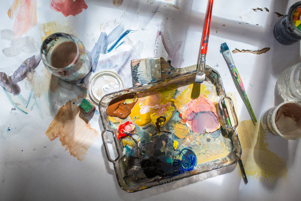 Palette and paint brush in artist hands. Artist paints oil picture with paint brush in hand palette close-up. Artist painting holding palette and paint brush in hand. Artists paintbrush with palette. - Photo, image