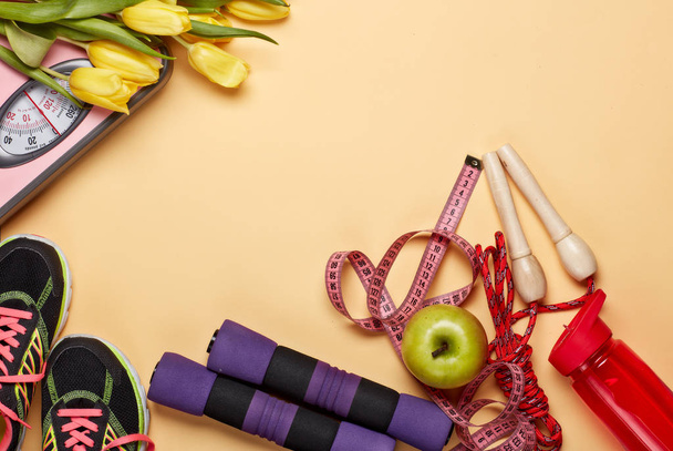 Female fitness still life. Sport accessories, tulips flowers and scales on a yellow background. Mockup. Planning of diet and trainings. Top view with copy space. Healthy lifestyle concept. Slimming - 写真・画像
