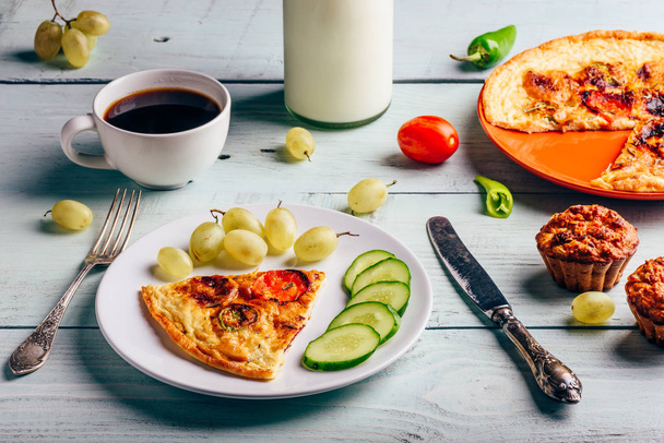 Breakfast frittata with chorizo, tomatoes and chili peppers on plate with cup of coffee, grapes and muffins over light wooden background. Healthy eating concept. - Fotó, kép