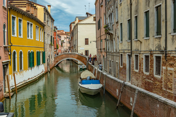 Venetië, Italië - 02 augustus 2019: Een van de duizenden gezellige hoekjes in Venetië op een heldere zonnige dag. Lokalen en toeristen slenteren langs de historische gebouwen en grachten met aangemeerde boten - Foto, afbeelding