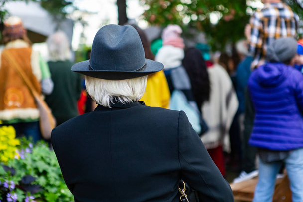 Vrouw met blazer en hoed die naar mensen kijkt - Foto, afbeelding
