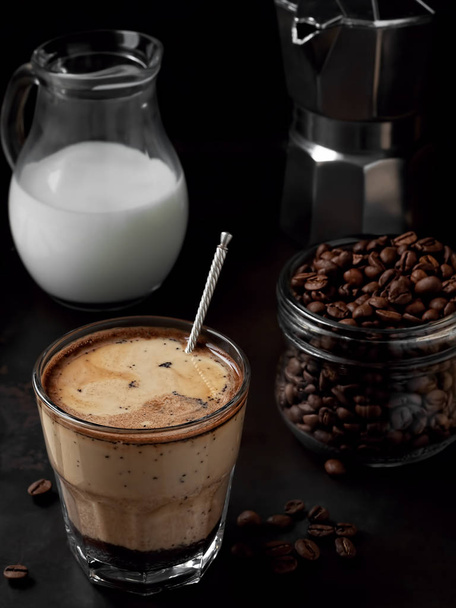 Café frío en un vaso con nata y granos de café sobre fondo de metal negro. Cerca de moka pot y jarra de leche. De cerca.
 - Foto, imagen