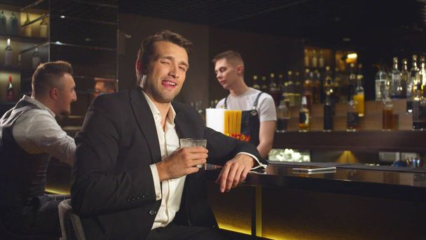 Slow motion, man drinkt alcohol aan de bar en kijkt glimlachend naar de camera - Foto, afbeelding