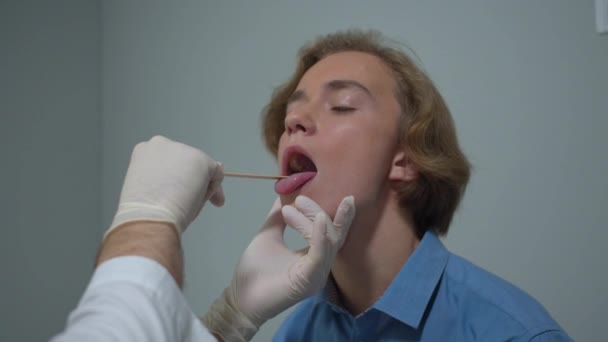 Boy sit in cabinet of hospital, doctor check his throat with stick - Materiał filmowy, wideo