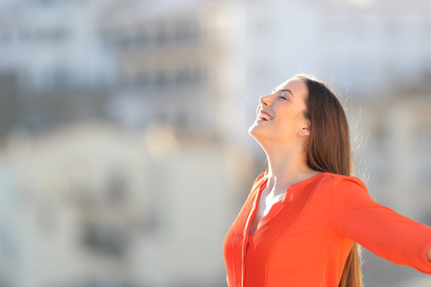 Side view portrait of a joyful woman in orange breathing deep fresh air outdoors in a town outskirts - Foto, Bild
