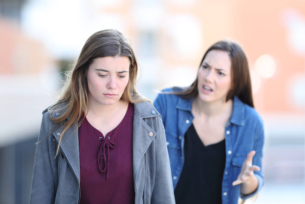 Angry girl scolding her stressed friend walking in the street - Foto, imagen