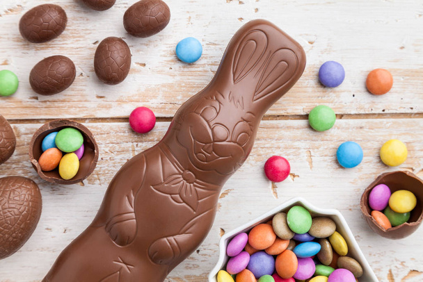 Delicious chocolate Easter bunny, eggs and sweets on rustic background - Fotó, kép