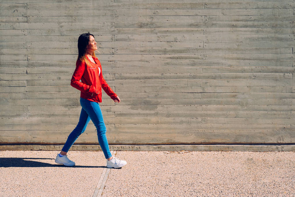 Millenial woman walking calmly in blue and red jeans next to a c - Photo, image