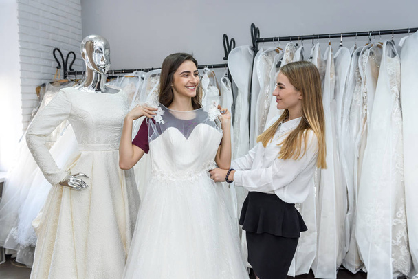 Schneiderin im Hochzeitssalon hilft Braut beim Anprobieren des Kleides - Foto, Bild