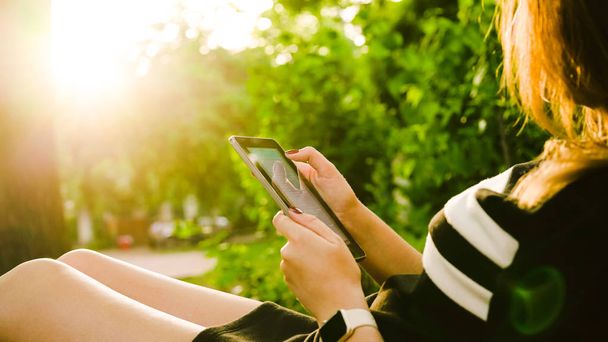 Dziewczyna w naturze czyta wiadomości z tabletu. słoneczny dzień w parku - Zdjęcie, obraz