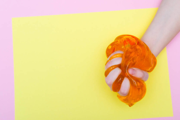 Child clutching colorful orange slime toy. Kids hands playing slime on yellow background. Making slime. Copyspace. top view. Flatlay - Zdjęcie, obraz