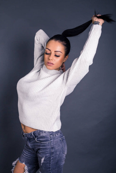 beautiful model posing in jeans and sweater against gray  - Фото, изображение
