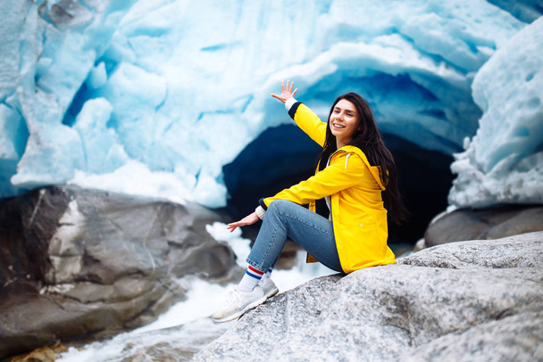 Woman hiking at glacier enjoys freedom. The girl tourist in a yellow jacket near a large glacier, a lot of ice. Cold tones. Travelling, lifestyle, adventure, concept. - Valokuva, kuva