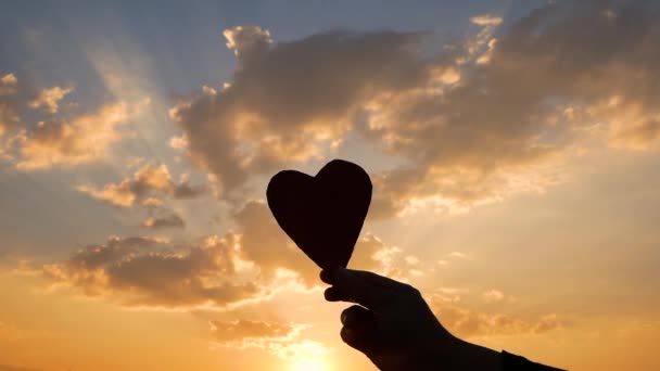 Silhouet van het hartvormige karton in de hand en de zon die door het hart schijnt op zonsondergang achtergrond. Begrippen liefde en Valentijnsdag. - Video