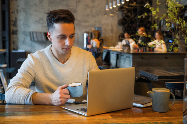 young man drinks tea and works on a laptop, freelancer working in a cafe - Foto, imagen