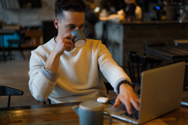 young man drinks tea and works on a laptop, freelancer working in a cafe - Fotografie, Obrázek
