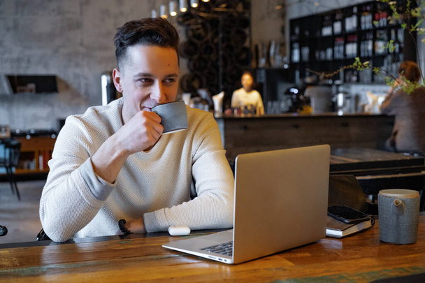 young man drinks tea and works on a laptop, freelancer working in a cafe - Foto, Imagem