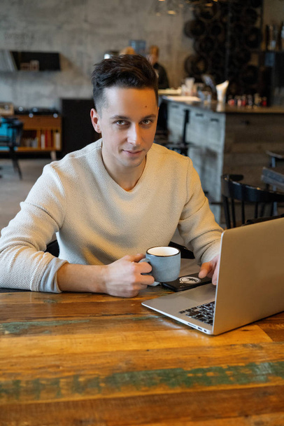 young man drinks tea and works on a laptop, freelancer working in a cafe - Fotoğraf, Görsel