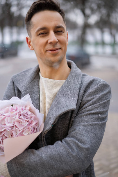 Boy friend with a bouquet of pink flowers hydrangea waiting for his girl friend outdoors while snow is falling. Valetnine`s day concept, wedding proposal. - Fotografie, Obrázek