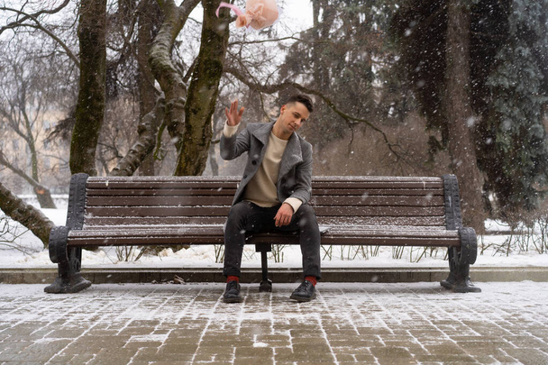 Boy friend with a bouquet of pink flowers hydrangea waiting for his girl friend outdoors while snow is falling. Valetnine`s day concept, wedding proposal. - Photo, image