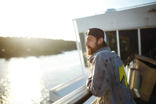 Guy enjoys a ferry ride or ship, sailing to the island tourist destination on summer vacation in sunny day. Styllish man is staring into the distance and joys the beautiful view. Travelling, lifestyle - Fotografie, Obrázek