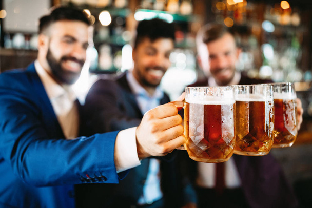 Happy handsome young businessmen drinking beer and talking at pub after work - Фото, изображение