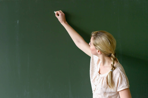 Female teacher writing with chalk on a chalkboard - Photo, Image