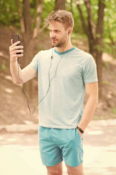 Phone designed for achieving fitness goals. Sportsman making video call from mobile phone outdoor. Athletic man using loudspeaker mode in his phone. Phone that keeps you connected everywhere - Фото, зображення